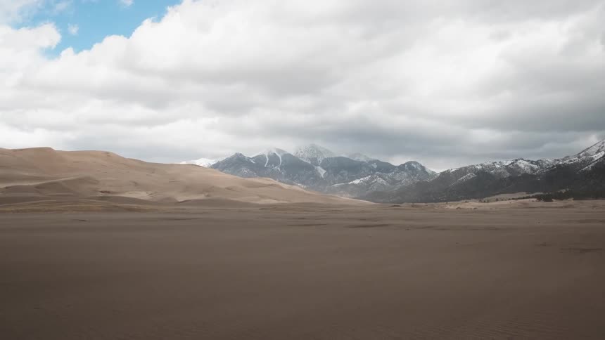View of sand dunes in front of snowy mountains