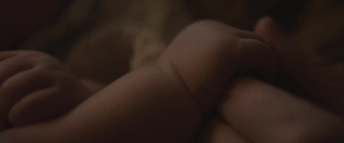 An infant's hand holding onto an adult's finger