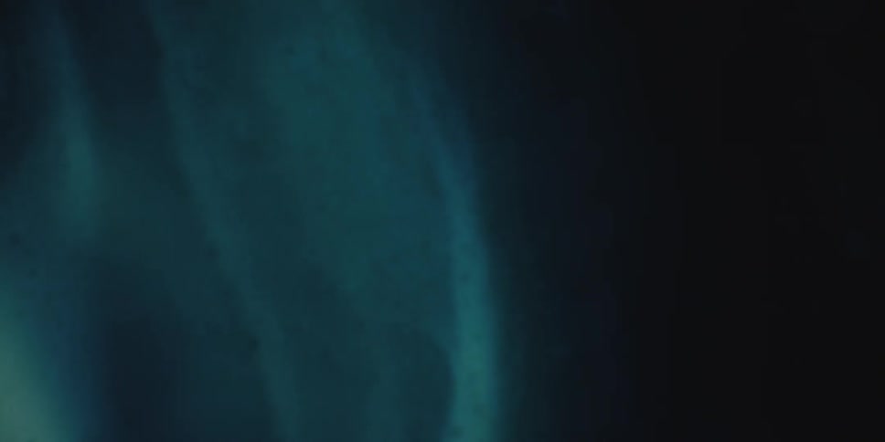 A blue fluidic substance slowly oozes while dimly lit from behind