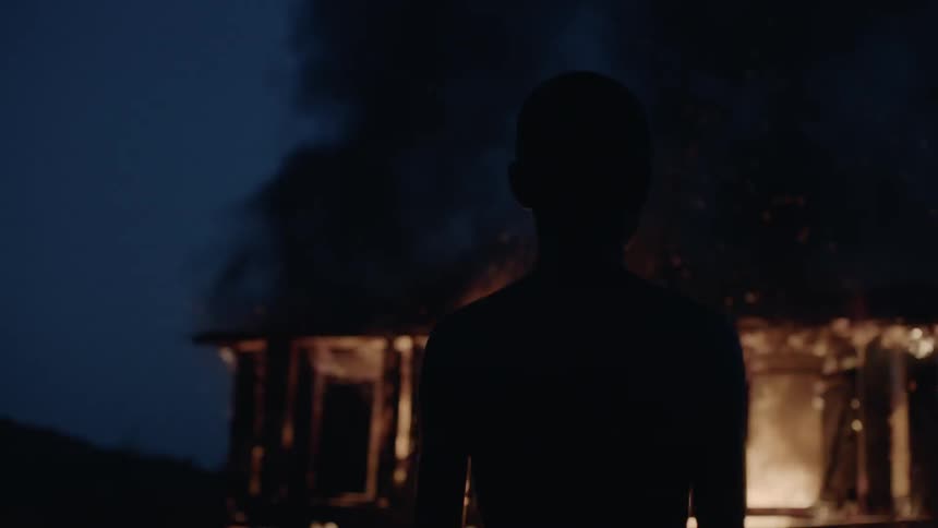 Child stands outside looking at a burning building at night