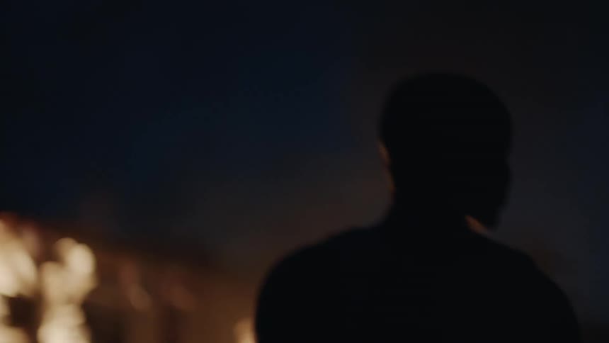 Man stands outside of a burning building at night