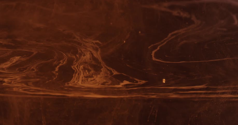 A white substance forms lines and swirls in a reddish brown substance
