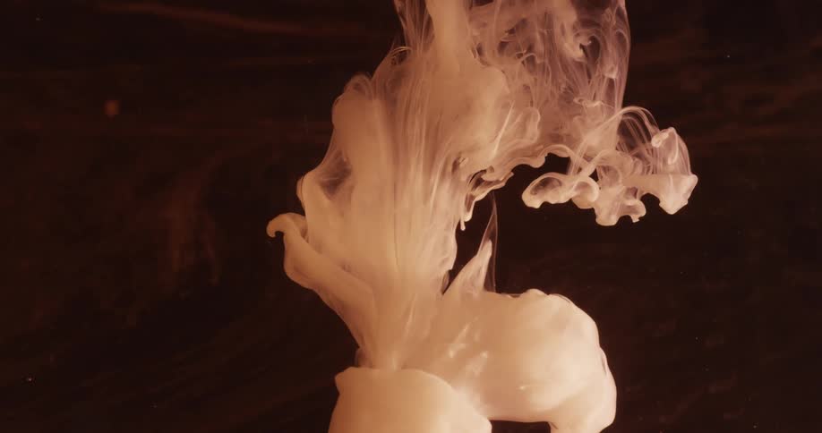 White liquid falling and forming smokey shapes against a dark background