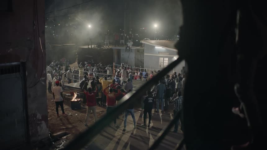Audience cheers while two people fight in a boxing ring