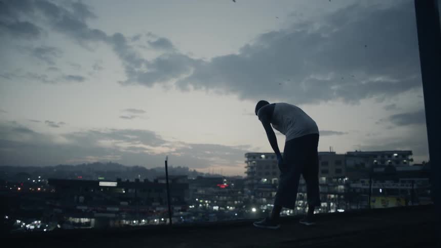 A man is leaning over and breathing heaving on a rooftop at dusk