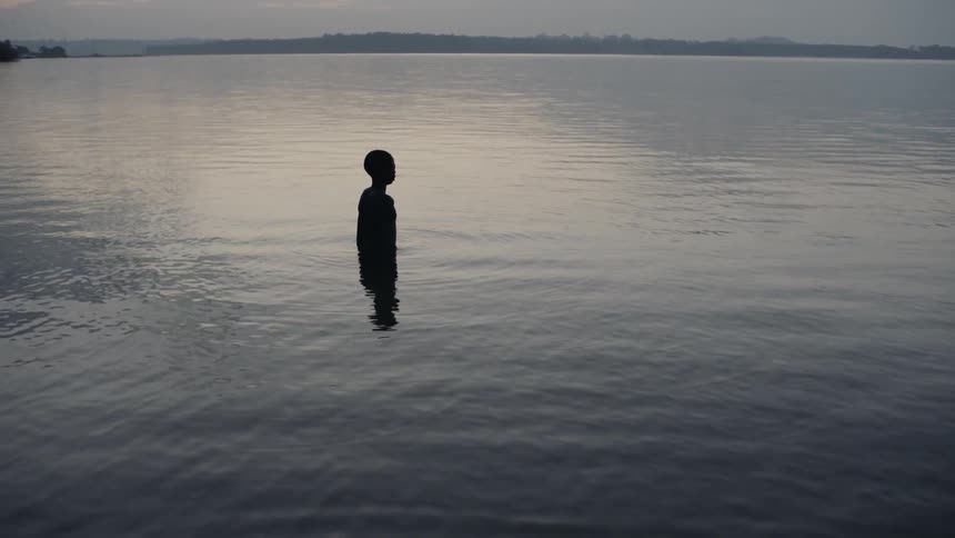 A boy stands in a lake at sunset