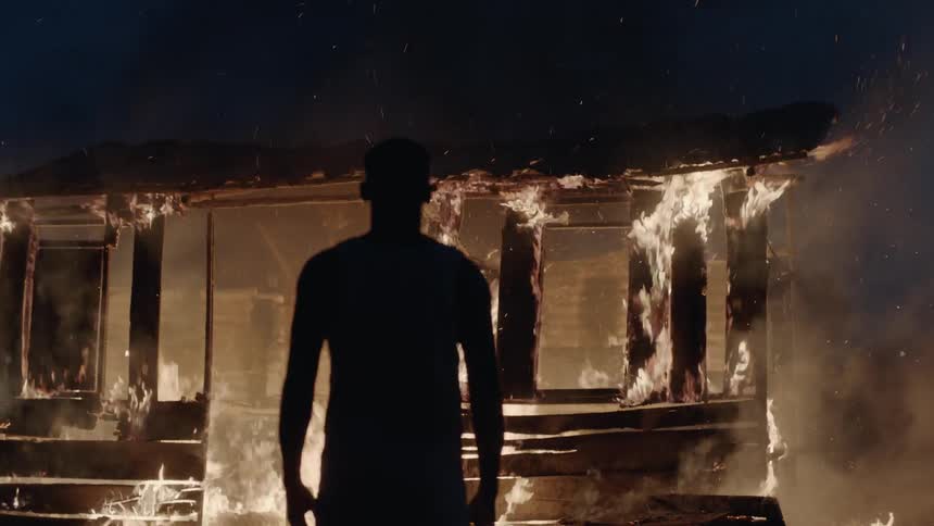 Man stands outside of a burning building at night
