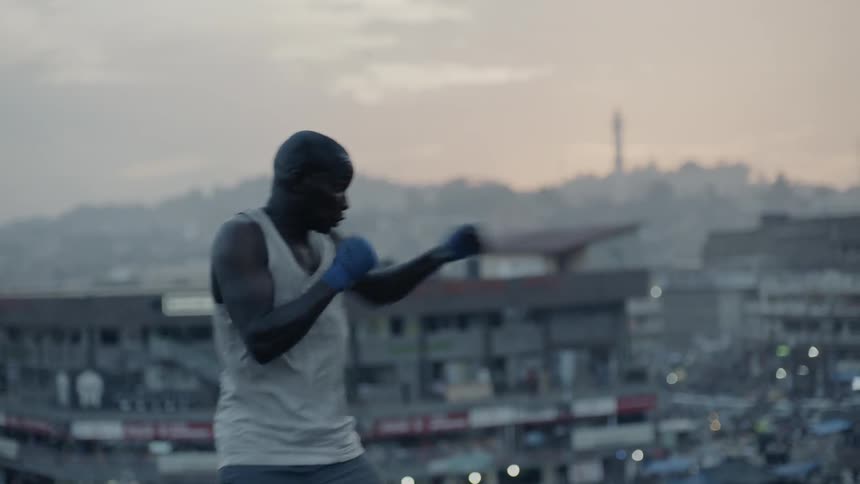 A boxer punches the air in a city at sunset