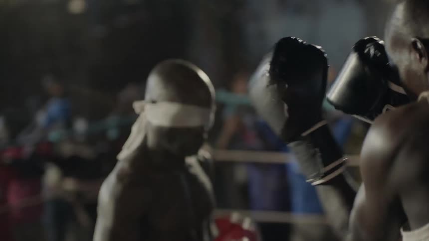 Two men box in a ring with an audience cheering behind them