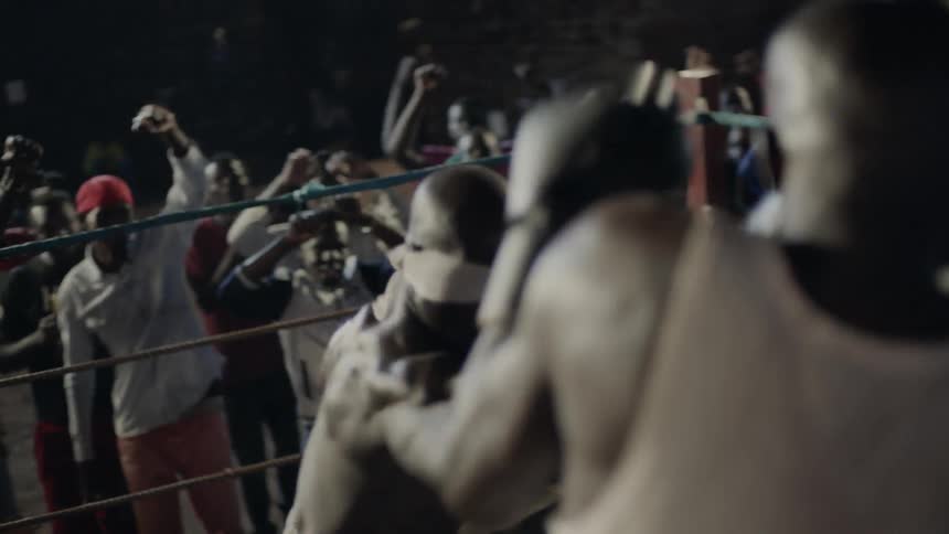 Two men box in a ring with an audience cheering behind them at night
