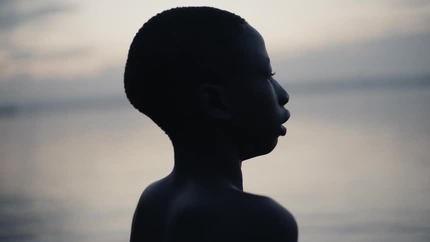 A boy stands in a lake at sunset