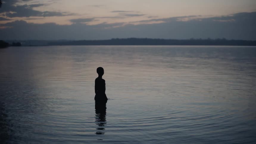 Child stands in a lake at sunset