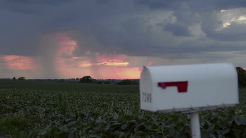 Rain falls over rural fields at sunset