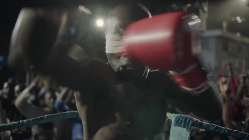 A boxer wearing a blindfold is taunting an opponent inside a ring at night