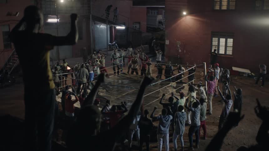Crowd cheers and looks down onto a boxing ring below