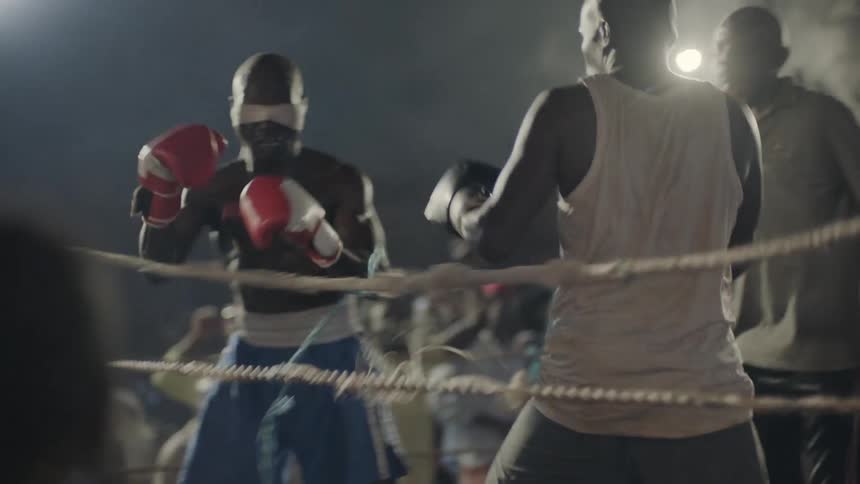 Two men box in a ring, one of them blindfolded and and audience cheers