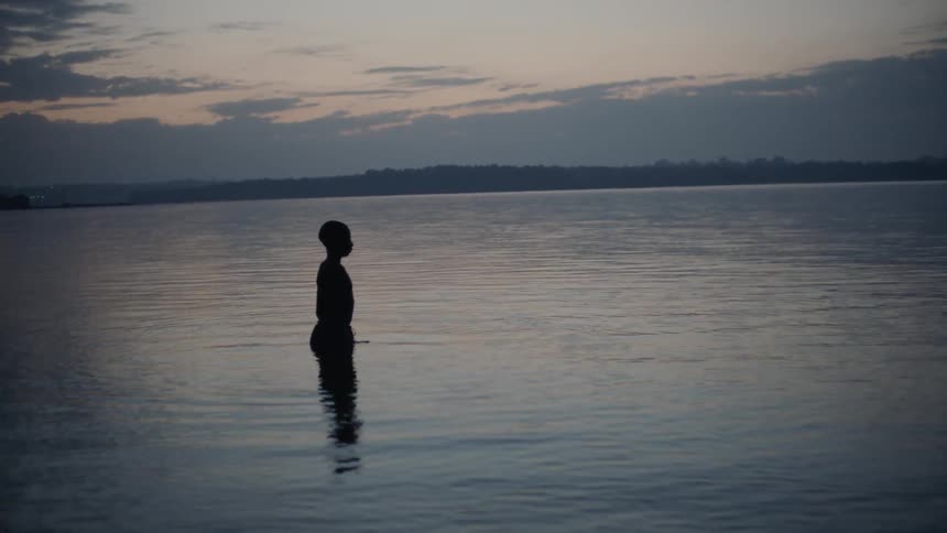 A boy stands in a lake at sunset