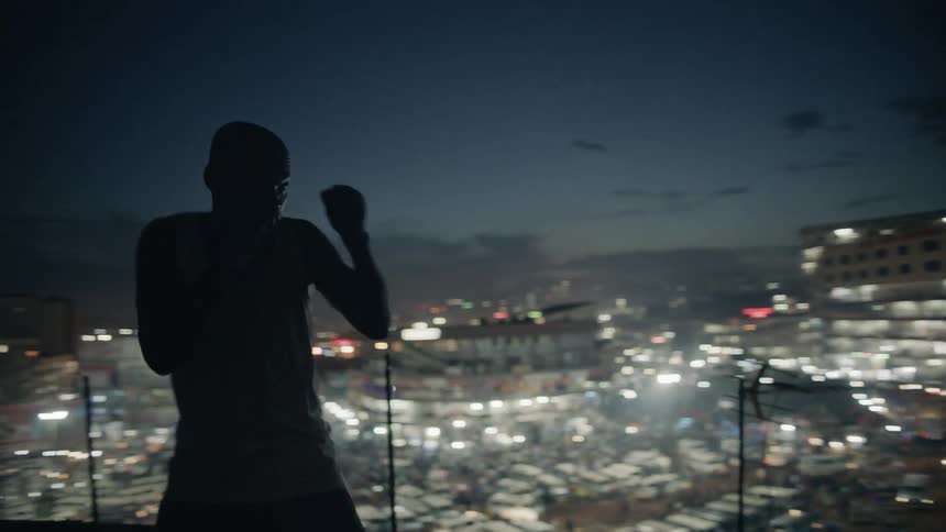A boxer punches the air on a building rooftop at night