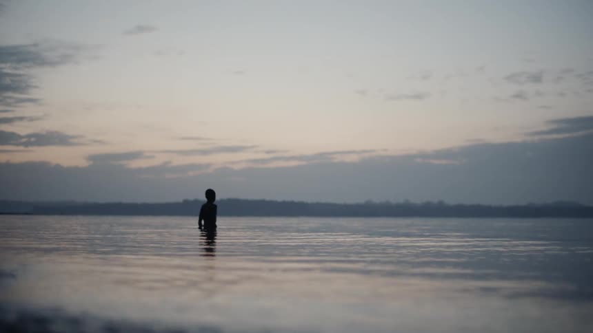 A boy stands in a lake at sunset