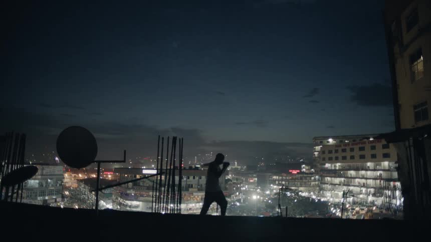A boxer punches the air on a building rooftop