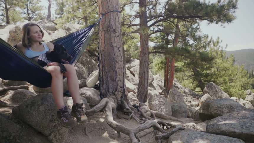 Woman and dog swing in a hammock in mountains