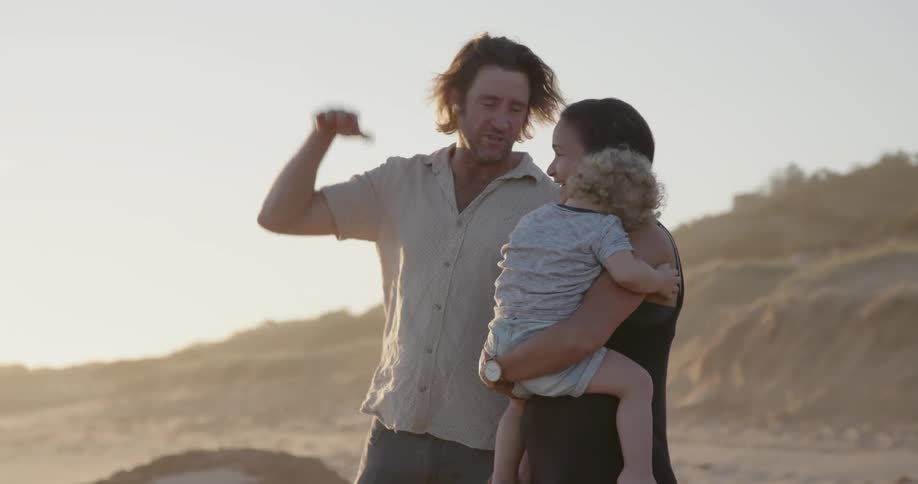 Man woman and child stand on the beach and the man smiles and gestures