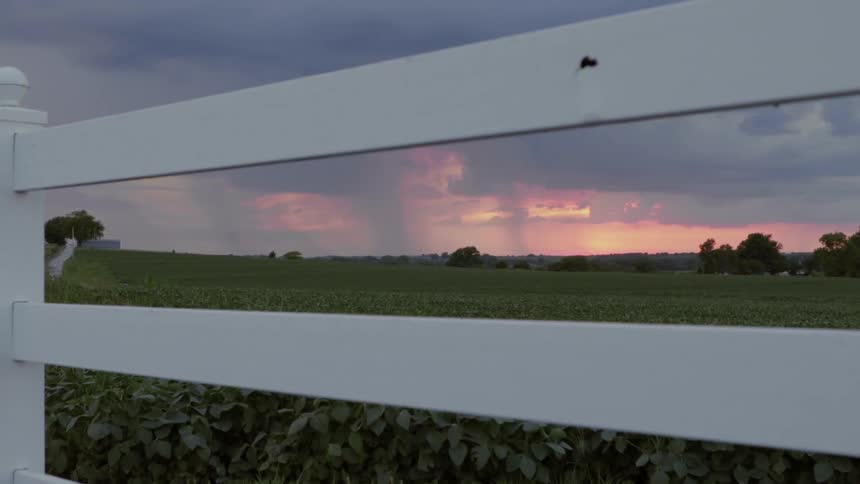 Rain falls from clouds over a rural area at sunset