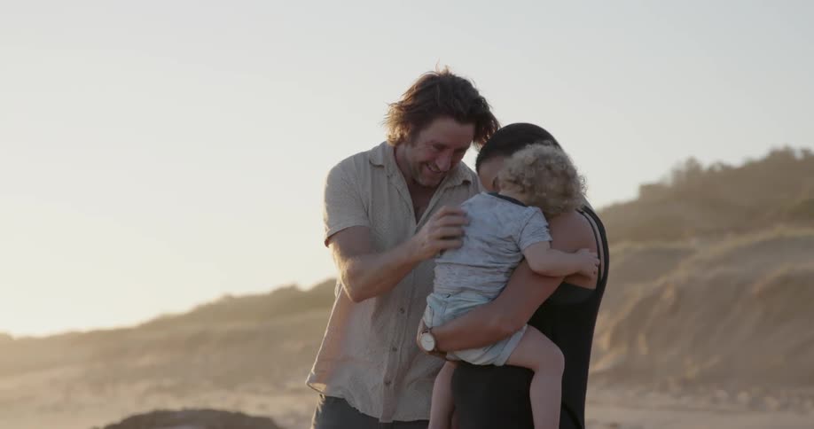 A young family stands on a beach at sunset