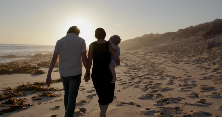 A young family walks on a beach at sunset