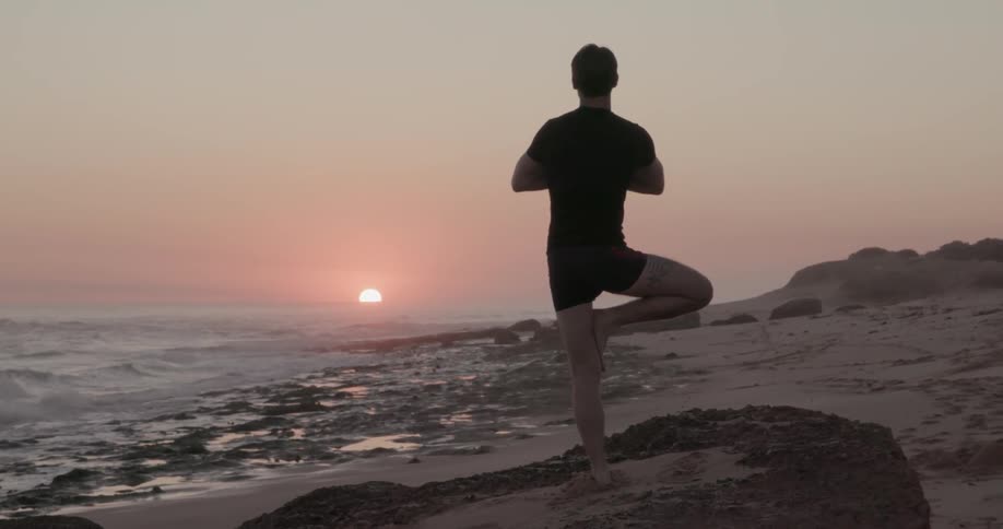 A man does yoga on a beach at sunset