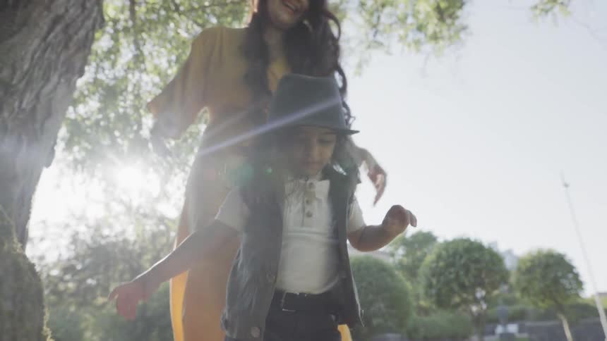 A young mother dancing behind her playful child during an outdoor picnic.