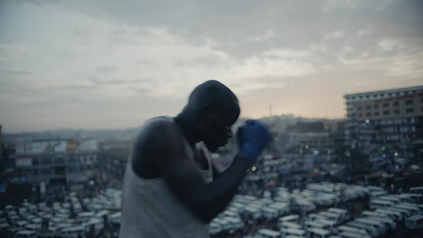 A boxer punches the air on a building rooftop at sunset