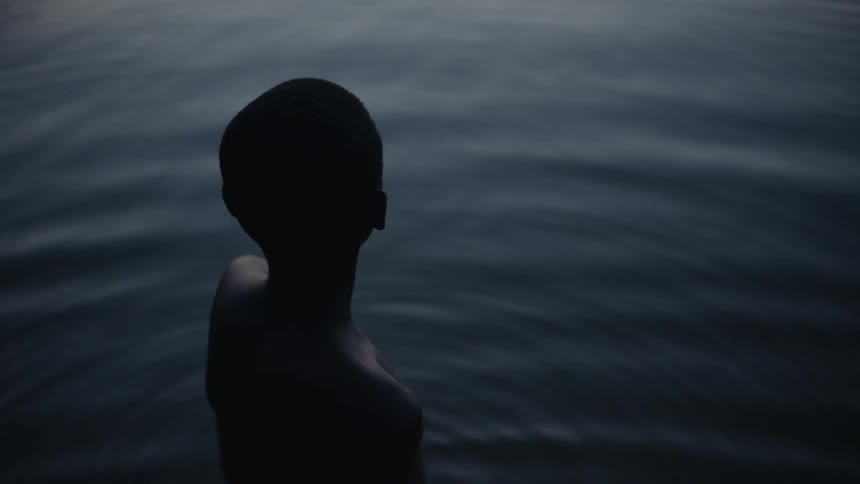 A boy stands in a lake at sunset
