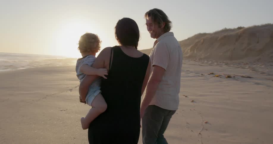 A young family walks on a beach at sunset