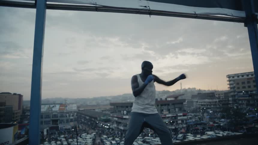 A boxer punches the air on a building rooftop at sunset