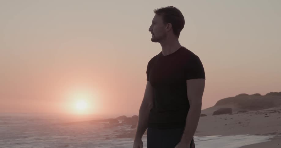 Man stands and looks around him as the sun sets in the distance