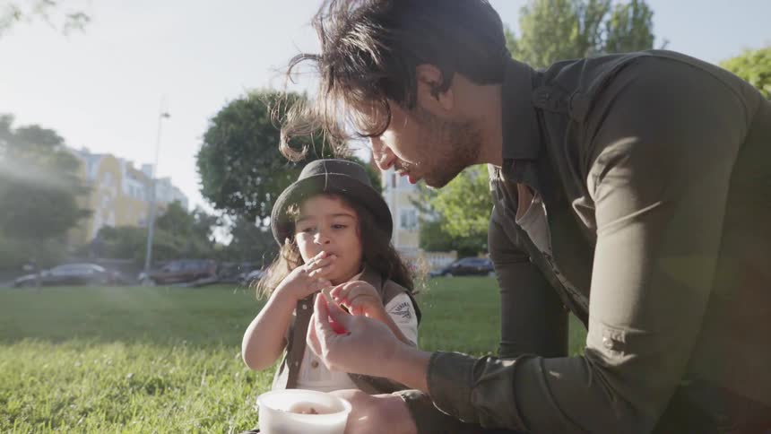 A young child eating snacks next to father during a family outdoor picnic.