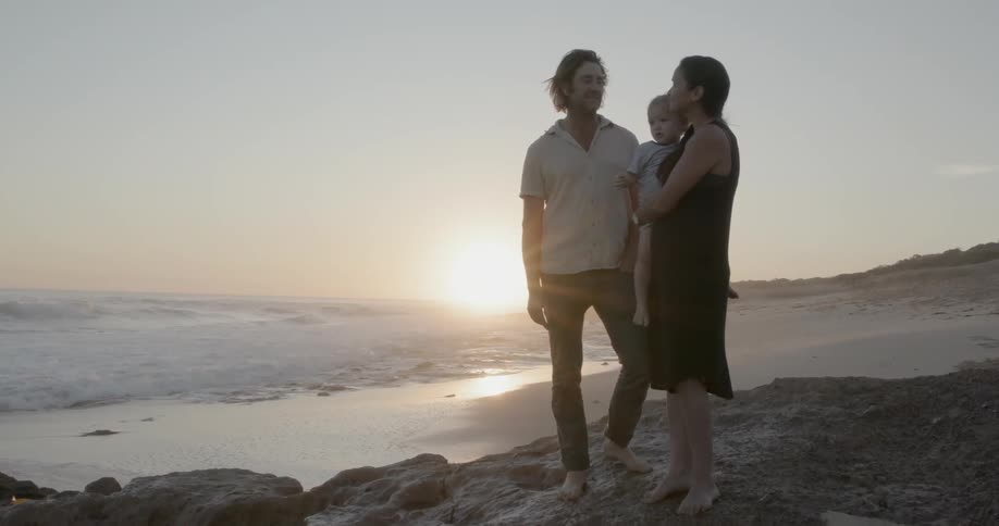 A young family stands on a beach at sunset