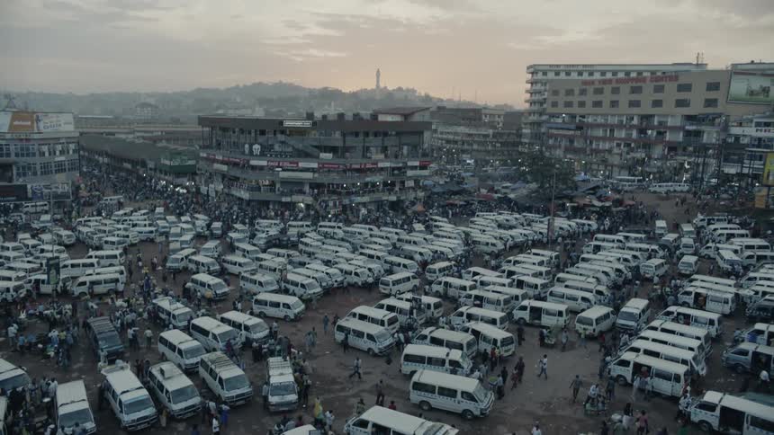 People are wandering through a parking lot filled with vans in a city near dusk