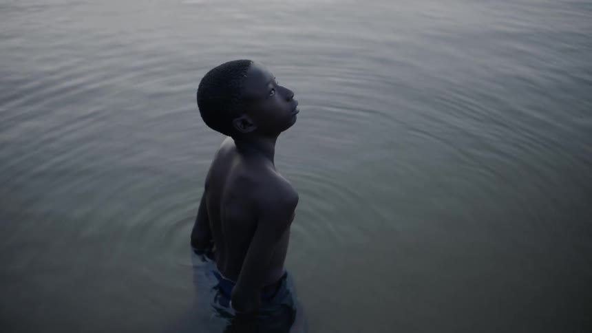 A boy stands in a lake at sunset