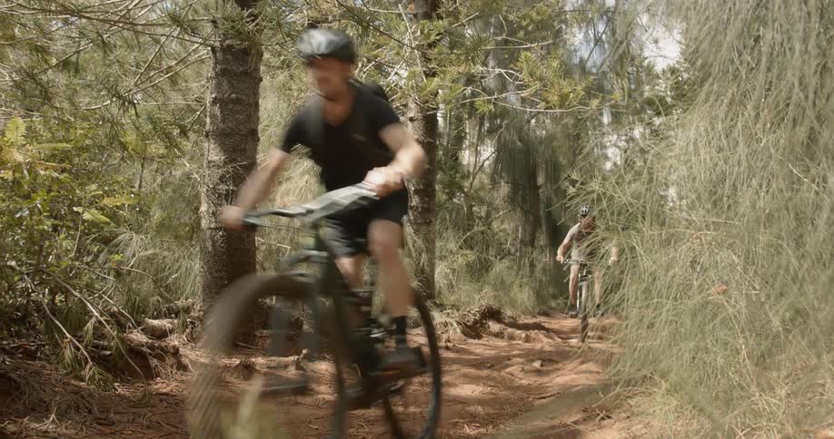 Two men are riding mountain bikes on dirt forest trail