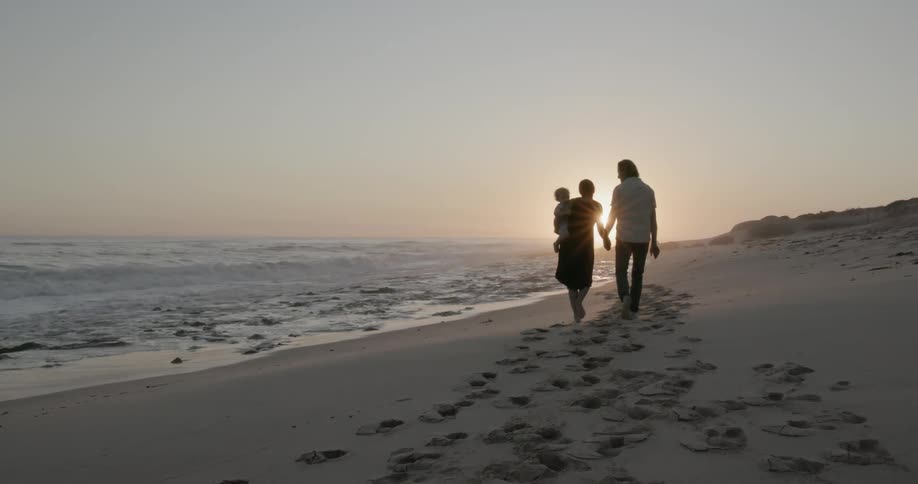 A young family walks on a beach at sunset