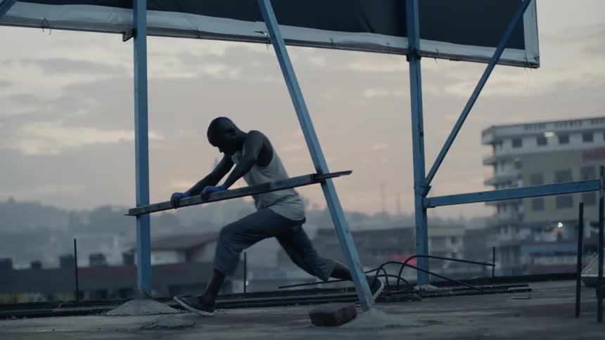 Man leans against a pole of a billboard on a rooftop stretching