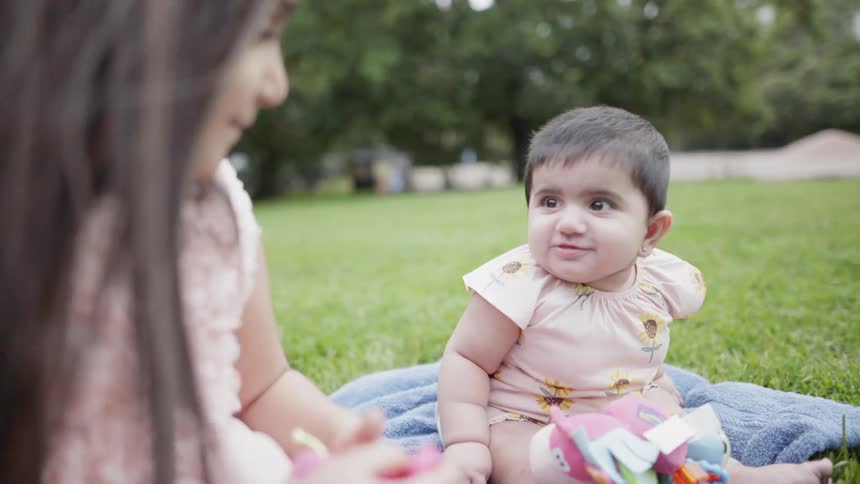 Baby on blanket in park plays with toy