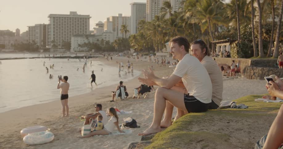 Two men talk on a beach at sunset