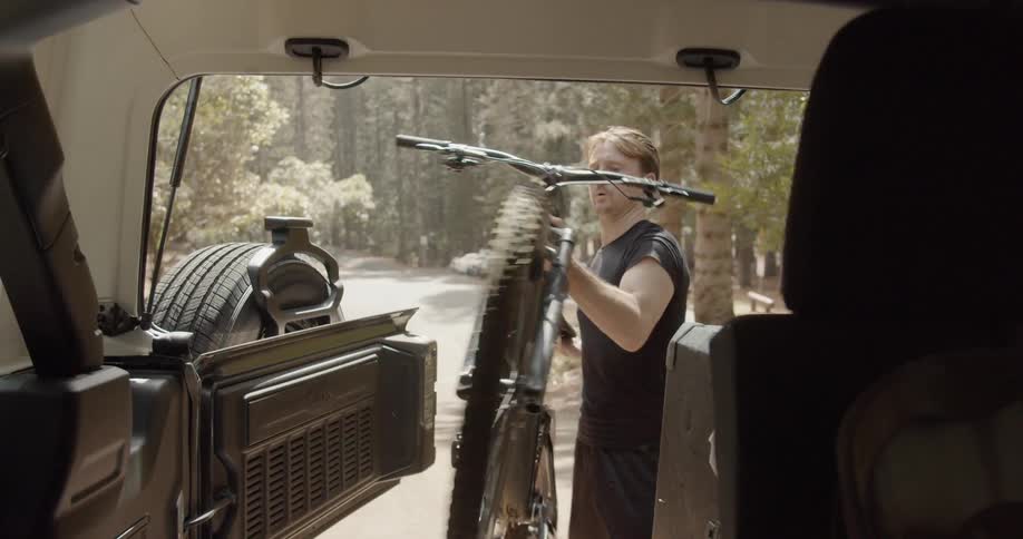 A man removes a bicycle from the back of a parked vehicle