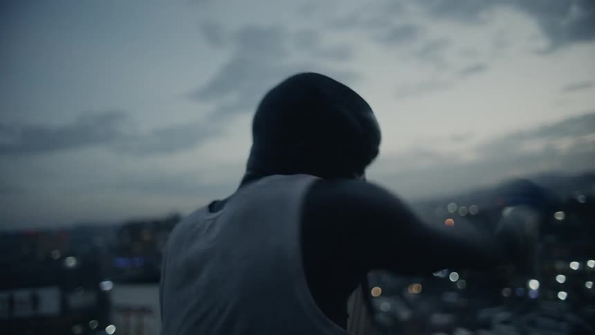 A boxer punches the air in a city at sunset