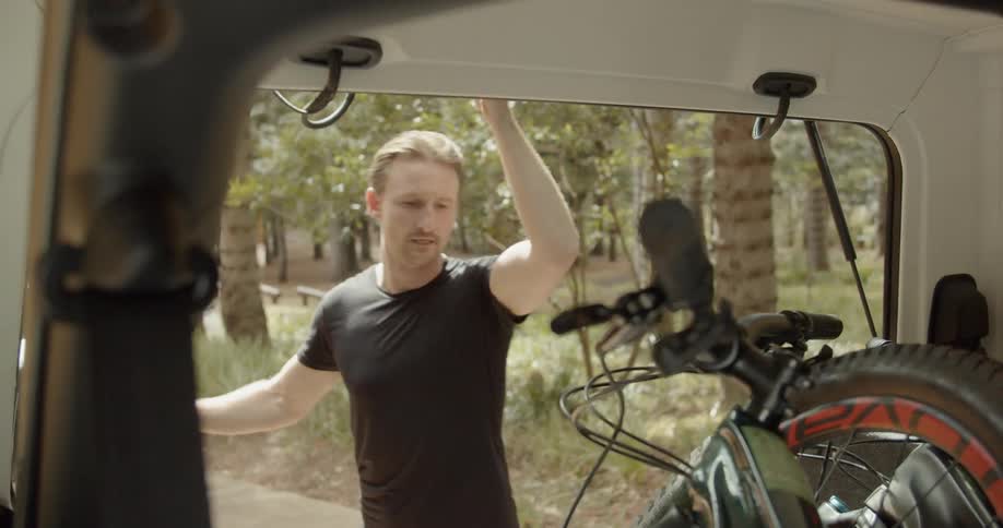 Man opens up the back of a jeep and takes a bike out
