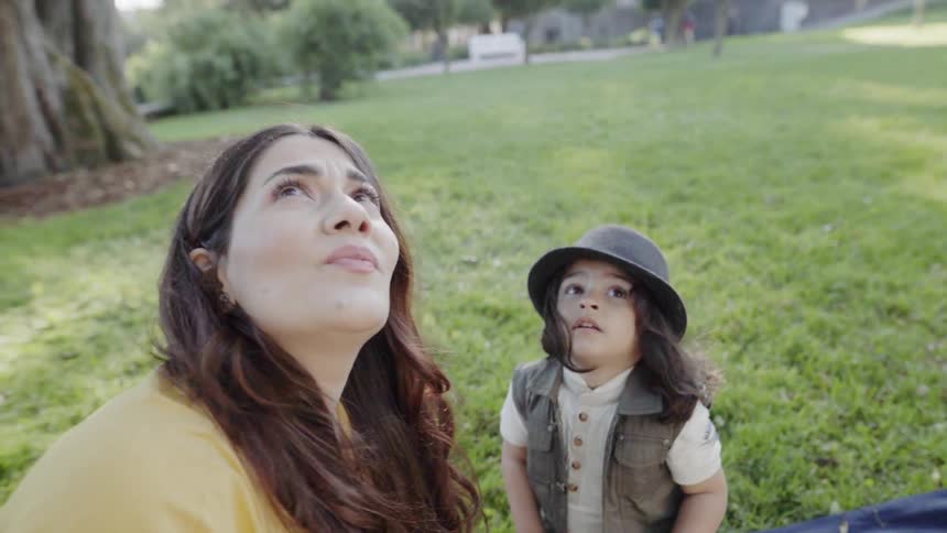 A young mother and child looking up together during an outdoor park picnic.