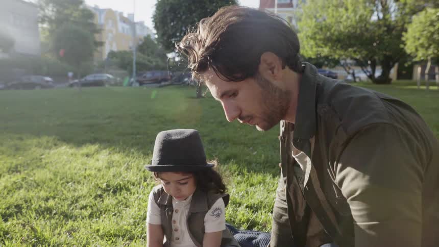 A father sitting on green grass outdoors spending quality time with child.